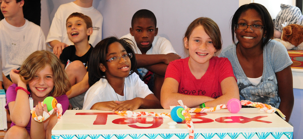 group of middle-school aged children surround a toy box they have decorated for animals