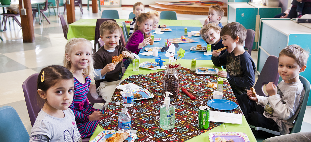 nine children seated at a long table eating pizza during a birthday party