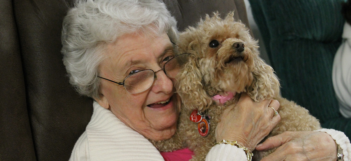 elderly woman smiles while embracing miniature poodle