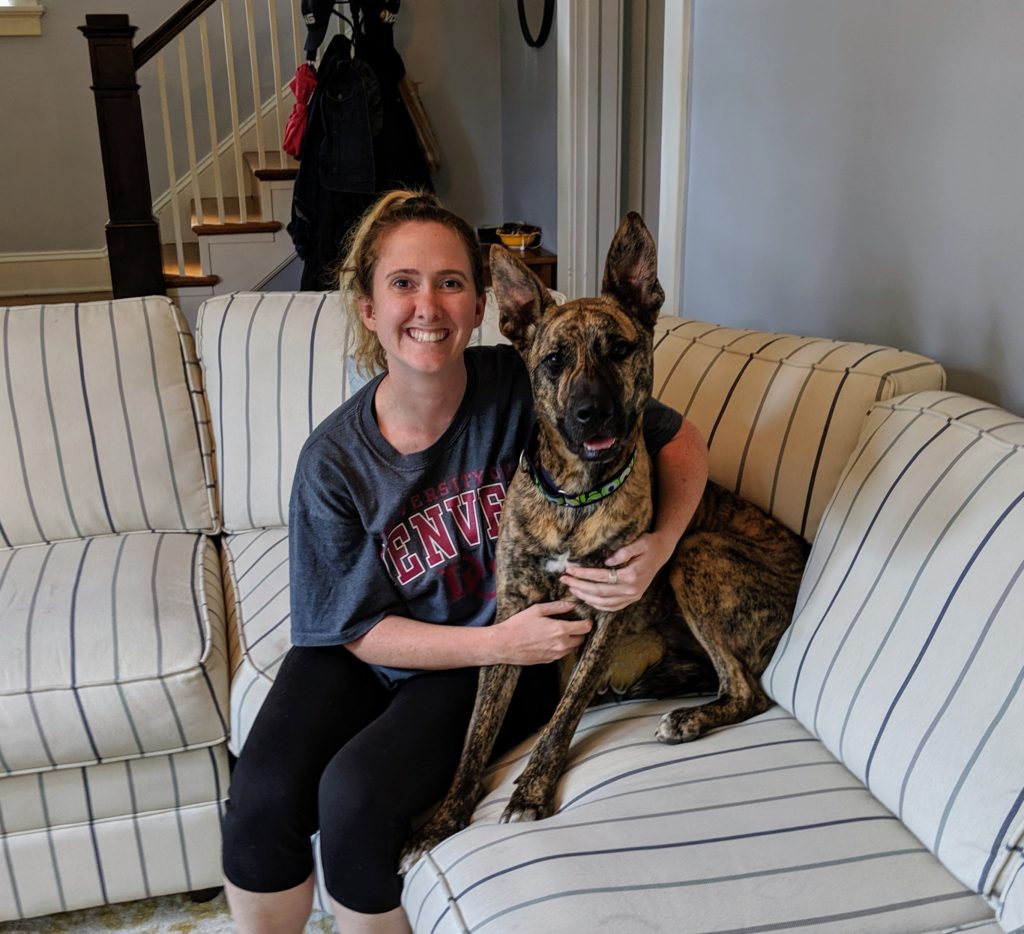 woman hugging a medium-sized brindle dog sitting on black and white striped sofa